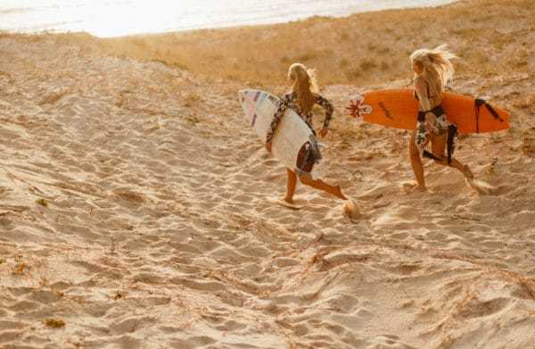 deux femmes passionnées de séjours sportifs prêtes à surfer sur la plage après un stage deméditation et de yoga